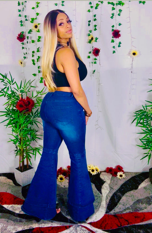 Model wearing blue casual flared wide leg pants and a black top in front of a floral and plant decorated wall.