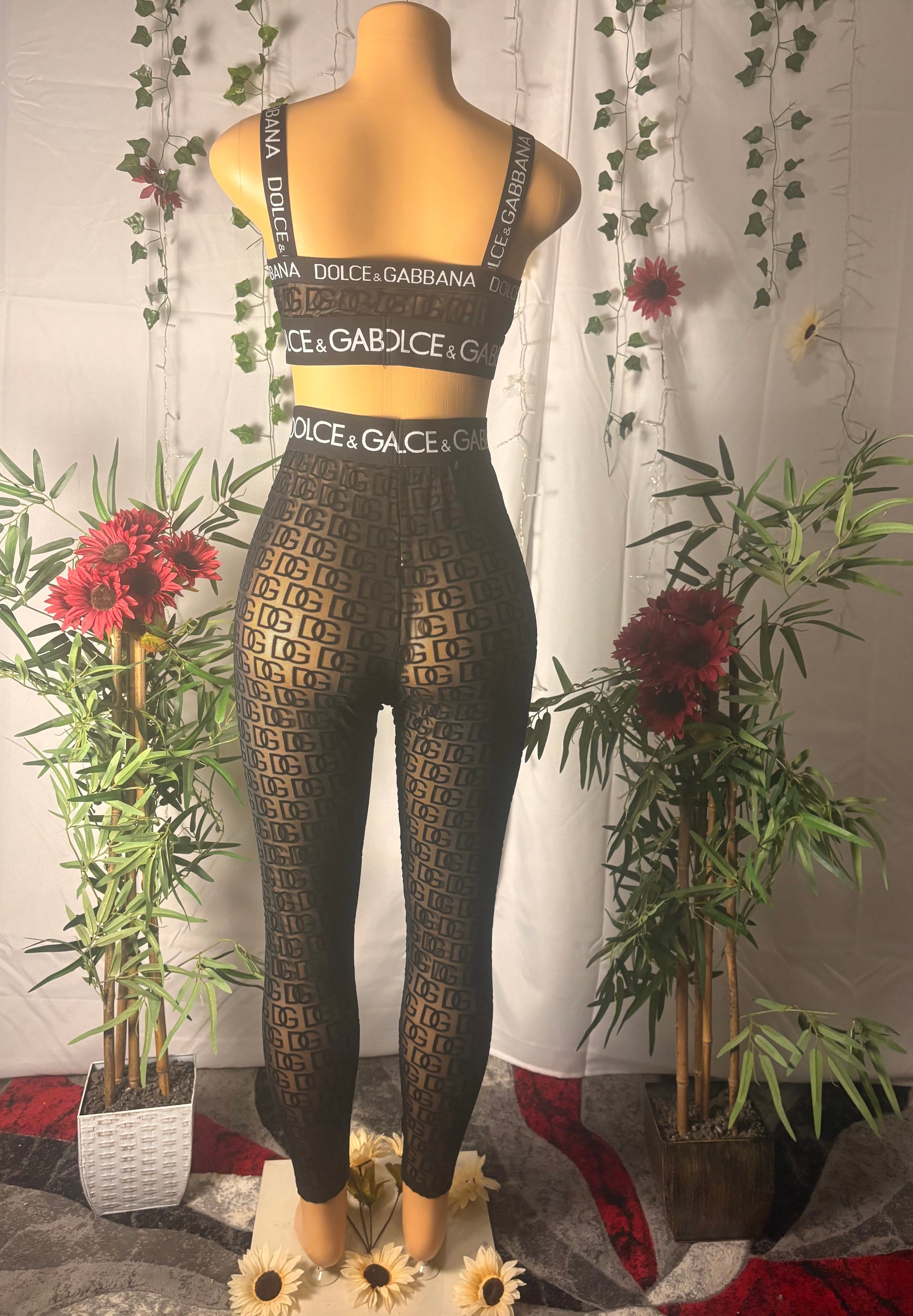 Mannequin wearing a two-piece mesh black laced patterned tights and sports bra with plants and flowers in the background