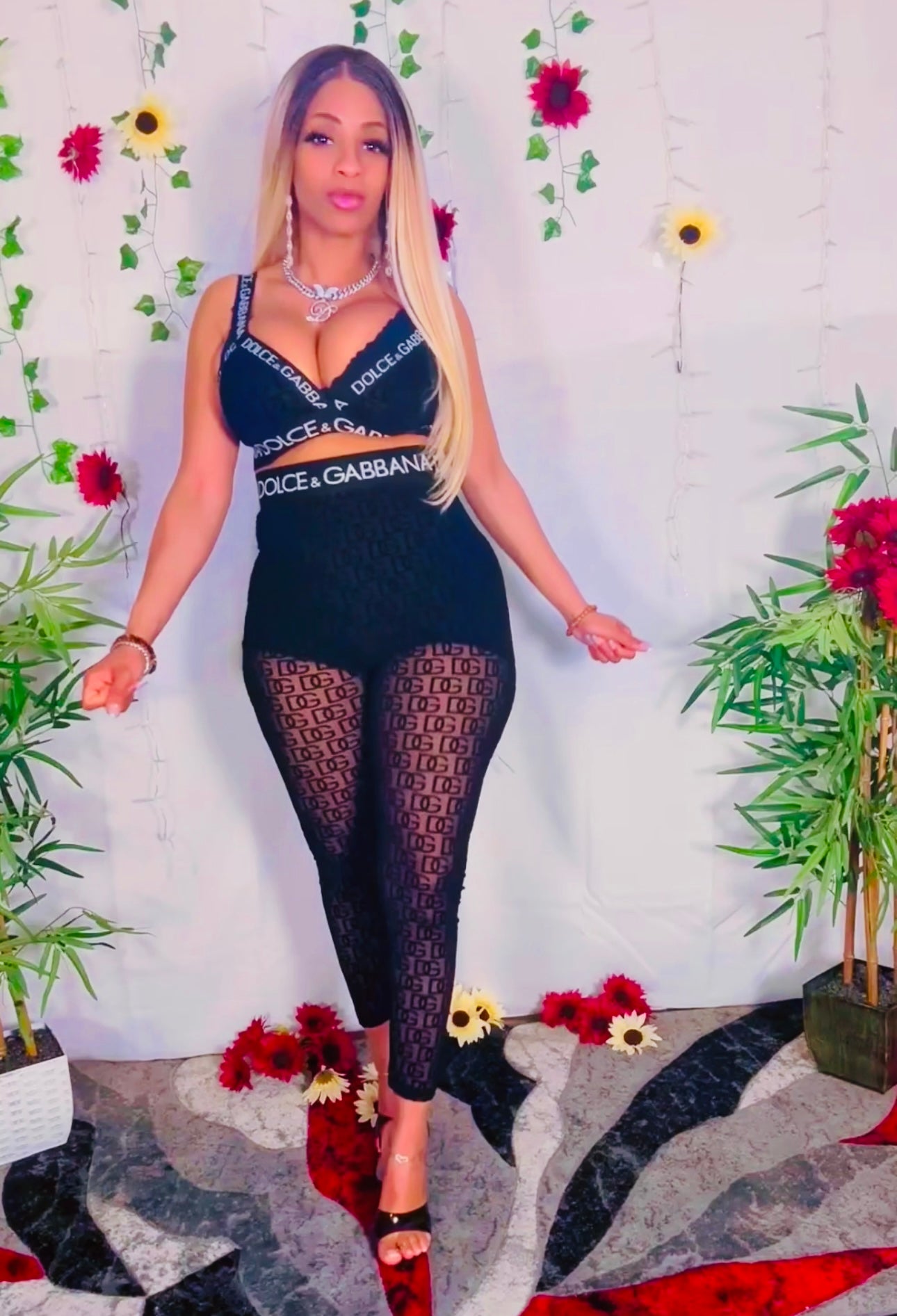 Woman wearing a sexy mesh black lace two-piece outfit with floral and plant decorations in the background