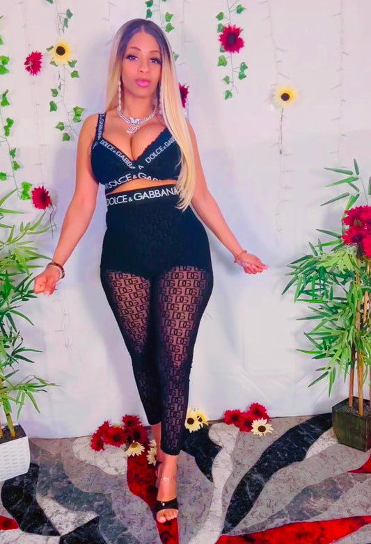 Woman wearing a sexy mesh black lace two-piece outfit with floral and plant decorations in the background